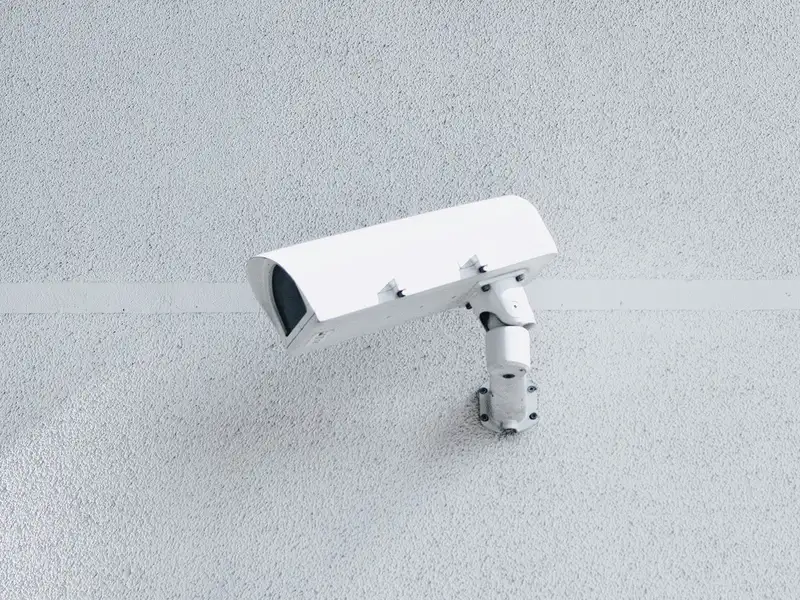 Caméra de vidéosurveillance blanche sur rotule, fixée en façade claire